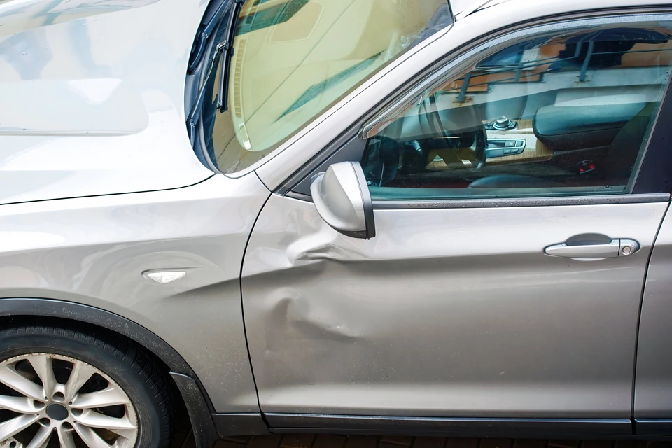 V&eacute;hicule automobile gris m&eacute;tallis&eacute; pr&eacute;sentant des dommages importants sur la porti&egrave;re conducteur et le montant de pare-brise, stationnement ext&eacute;rieur sur surface asphalt&eacute;e