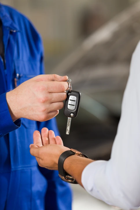 Sc&egrave;ne ext&eacute;rieure de remise de cl&eacute;s automobiles entre deux personnes pr&egrave;s d'un v&eacute;hicule blanc