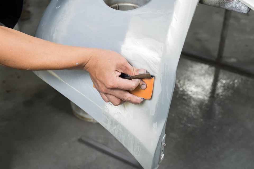 Atelier de carrosserie automobile intérieur avec ouvrier masqué appliquant peinture rouge sur carrosserie de véhicule