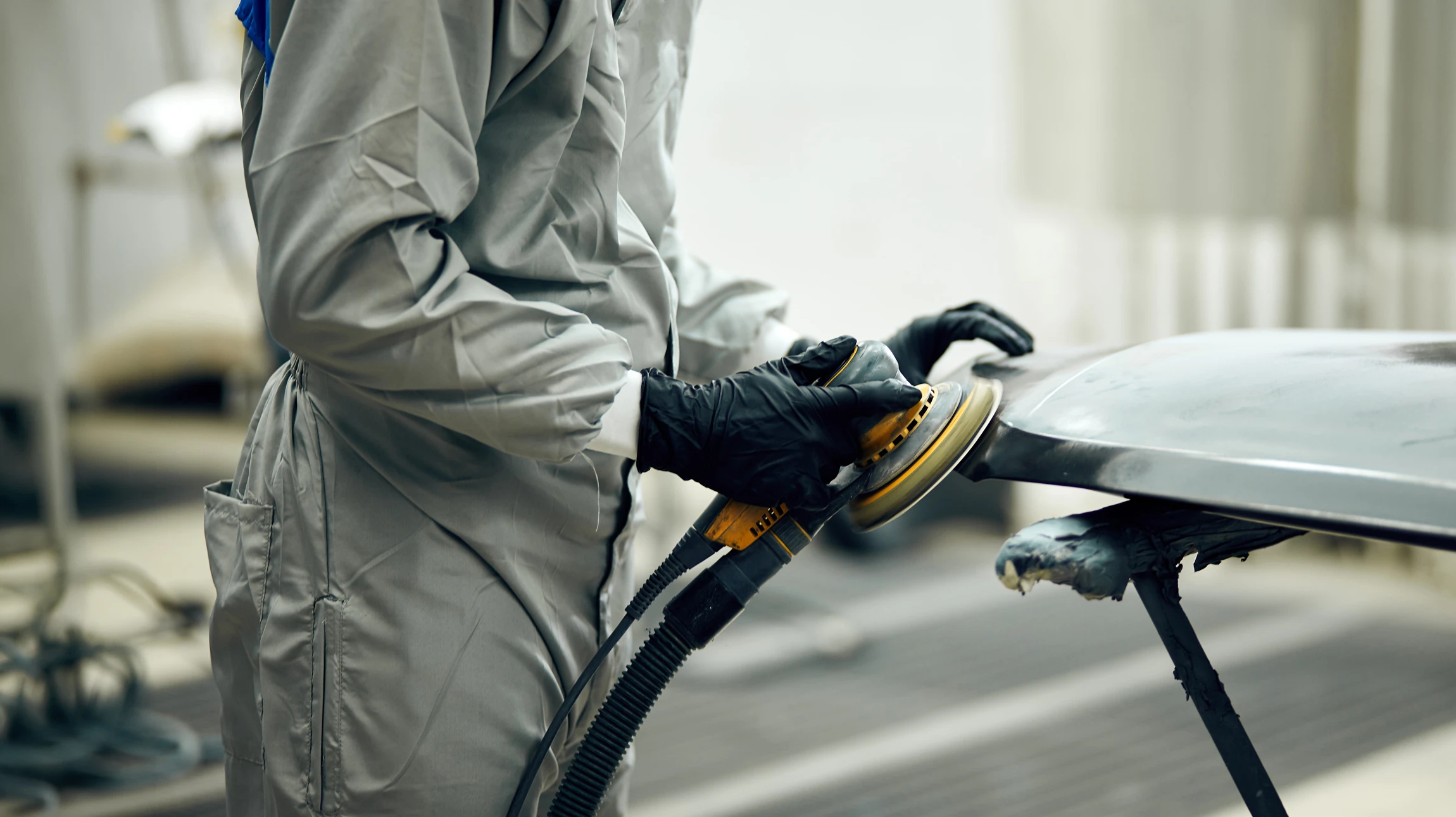 Atelier de carrosserie automobile professionnel où deux techniciens en combinaisons appliquent de la peinture au pistolet sur une voiture partiellement masquée